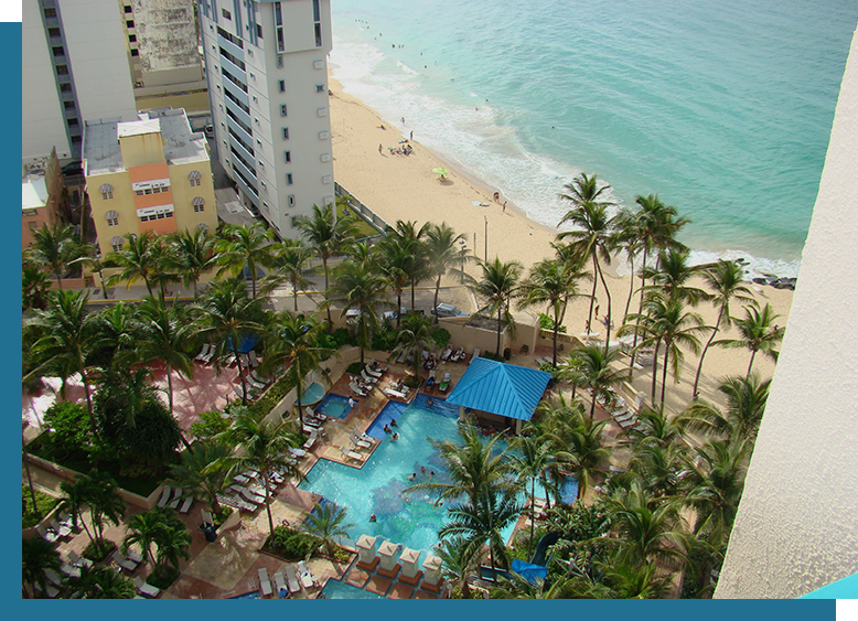 A view of the ocean from above shows palm trees, an outdoor pool and beach.